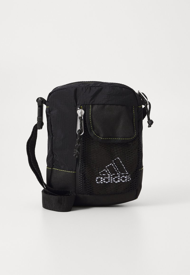 Černá nylonová crossbody taška s přední kapsou ze síťoviny, stříbrnými detaily, limetkovými akcenty a nastavitelným popruhem. Na tašce se nachází logo Adidas.