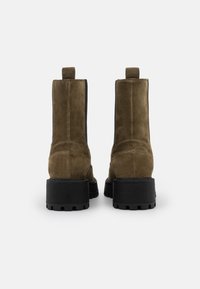 Zamszowe botki na kostkę w oliwkowej zieleni o teksturowanym wykończeniu, z solidną czarną gumową podeszwą i pętlami do ściągania z tyłu.