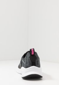 Baskets tricotées noires et grises avec une semelle blanche rembourrée, présentant un logo rose sur la languette et des accents noirs au niveau du talon.