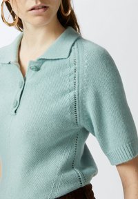 Svijetloplava kratko rukava pamučna polo majica s ovratnikom, zatvaranjem na gumbe, teksturiranim detaljima uz šavove i mekanim završetkom.