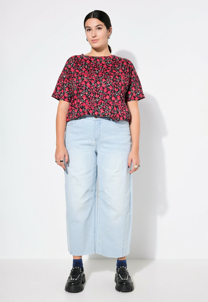 Blommönstrad svart topp med kort ärm och röda blommor, kombinerad med ljusblå vida jeans och kraftiga svarta platåskor.