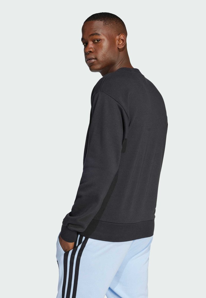 Sort crewneck sweatshirt med en afslappet pasform, der har lange ærmer og ribbede manchetter, sammen med lyseblå sportsbukser med sorte striber.