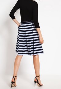Maglia nera a maniche lunghe abbinata a una gonna a righe blu navy e azzurro chiaro, lunghezza ginocchio, con plissè. La modella indossa sandali neri con tacco alto.