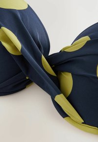 Navyblått tyg med stora gula prickar, som visar en mjuk textur och slät yta. Tyget är elegant tvinnat.