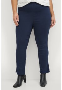 Navy blue pants in stretchy material, tailored fit with side slits at the hem, paired with black ankle boots.