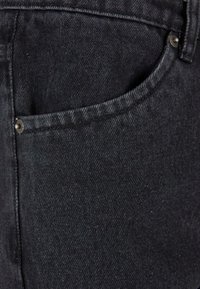 Jeans de mezclilla negra con un bolsillo frontal con cierre de botón metálico, mostrando una tela texturizada y ligeramente desgastada.