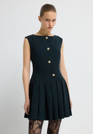 Robe bleu marine avec un corsage ajusté, une jupe plissée et des boutons dorés. Manches courtes et encolure ronde. Collants en dentelle noire texturée.