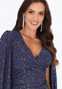 Navy Kleid mit glitzernden silbernen Punkten, Wickeldesign, tiefem V-Ausschnitt und langen Puffärmeln. Funkelnde Ohrringe setzen Details.