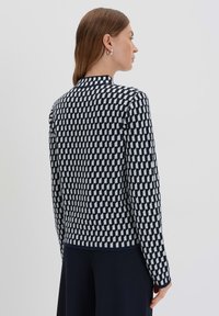 Navy- und weiß gemusterter Strickpullover mit hohem Kragen, ausgestattet mit einem geometrischen Design und langen Ärmeln, von hinten betrachtet.