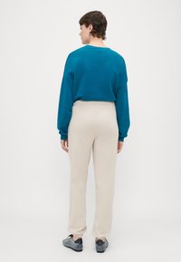 Teal oversized sweatshirt, beige tapered pants, grijze sneakers. Glad materiaal, ontspannen pasvorm, omgeslagen broekspijpen, eenvoudig ontwerp, geen patronen.