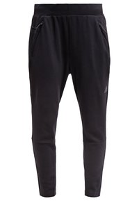 Černé tapered joggery vyrobené z měkké tkaniny s elastickým pasem, potažené dvěma bočními zipovými kapsami a diskrétním logem na noze.