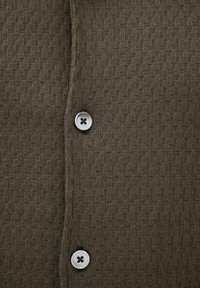 Primo piano di tessuto marrone con motivo intrecciato e due bottoni bianchi a quattro fori allineati verticalmente.