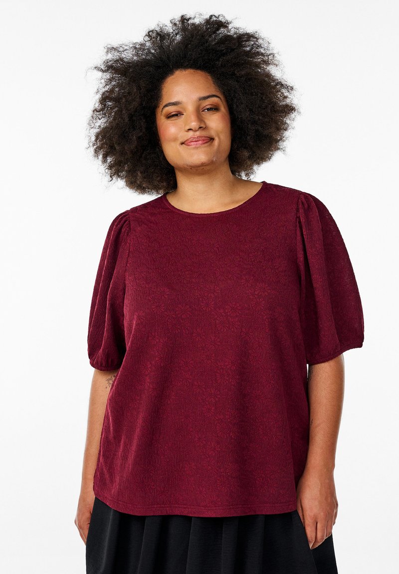 Burgundy kortärmad topp med ett strukturerat blommönster och rund halsringning. Ligger löst och har puffärmar som framhäver komfort.