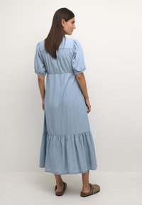 Ljusblå denimklänning med puffärmar, en figursydd liv och en tiered volangkant, som erbjuder en mjuk textur och avslappnad silhuett.