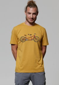 Geel T-shirt met korte mouwen met een afbeelding van een tandemfiets, met een rode frame, bruine leren zittingen en een gedetailleerd wielontwerp.