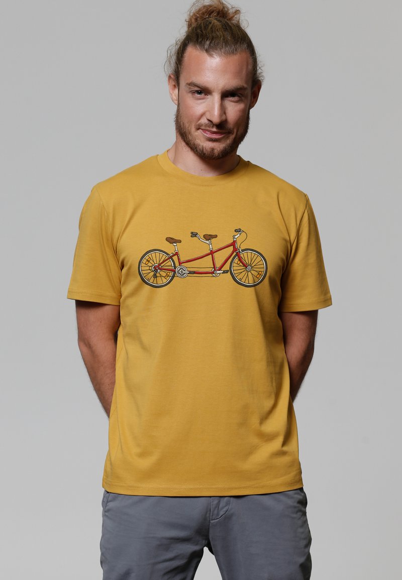 Geel T-shirt met korte mouwen met een afbeelding van een tandemfiets, met een rode frame, bruine leren zittingen en een gedetailleerd wielontwerp.