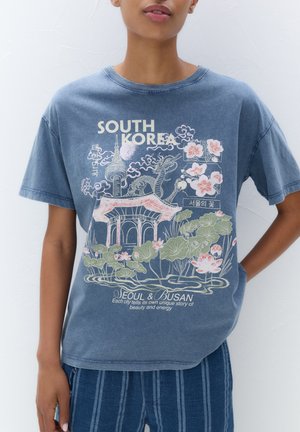 T-shirt in cotone blu con una grafica che rappresenta una pagoda, fiori e la scritta "COREA DEL SUD", maniche corte e vestibilità rilassata.