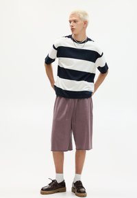 Striped t-shirt in navy and white, relaxed fit; paired with knee-length mauve shorts; black lace-up shoes with thick soles.
