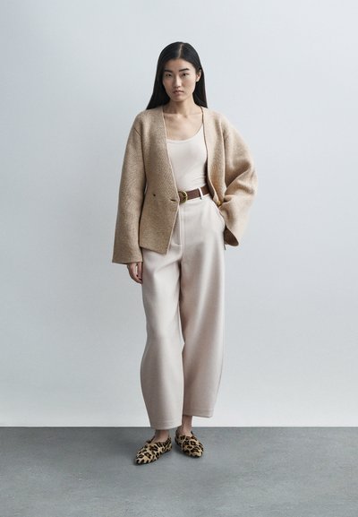 Μπεζ πλεκτή ζακέτα πάνω από μπεζ τοπ, συνδυασμένη με ανοιχτόμπεζ παντελόνι. Διακοσμημένη με καφέ ζώνη και παπούτσια με λεοπάρ μοτίβο.