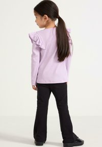 Lilla langærmet skjorte med rynkede skuldre, parret med sorte flared bukser og sorte sko. Glat stof og enkelt design.