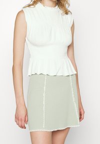 Weißes, geripptes Cropped-Top mit einem Fransen-Ausschnitt, kombiniert mit einem hellgrünen, strukturierten Minirock, der mit weißen, gekerbten Details verziert ist.