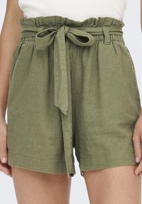 Pantaloni corti verdi in lino con cintura in tessuto, vita elasticizzata e tasche laterali. La trama è morbida e leggermente stropicciata, offrendo un design informale.