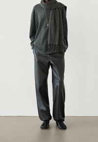 Pull en maille gris foncé à épaules tombantes, associé à un pantalon en cuir noir taille haute. Écharpe épaisse grise avec détails en franges. Bottines noires.