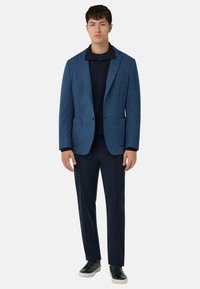 Niebieska teksturowana marynarka na granatowej koszulce polo, w zestawieniu z granatowymi spodniami i czarnymi trampkami. Posiada dwie przednie kieszenie i klasyczne dopasowanie.