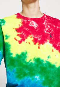 Färgglad tie-dye sweatshirt med livliga mönster i röd, gul, grön och blå. Den har en rund halsringning och ribbade detaljer.