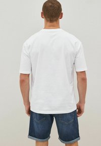 Biała bawełniana koszulka z krótkim rękawem, okrągłym dekoltem i gładką fakturą, połączona z niebieskimi szortami dżinsowymi z podwiniętymi nogawkami.