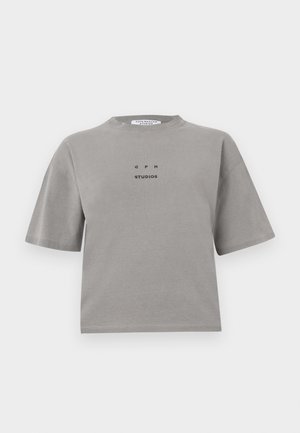 T-shirt en coton gris à manches courtes, avec un col rond et un logo sur le devant indiquant "GPH STUDIOS" en noir. Conception à coupe détendue.