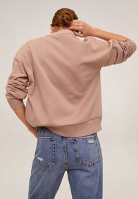 Beżowy, teksturowany sweter z okrągłym dekoltem i ściągaczami przy rękawach, w połączeniu z niebieskimi, zniszczonymi dżinsami. Widok z tyłu na strój.