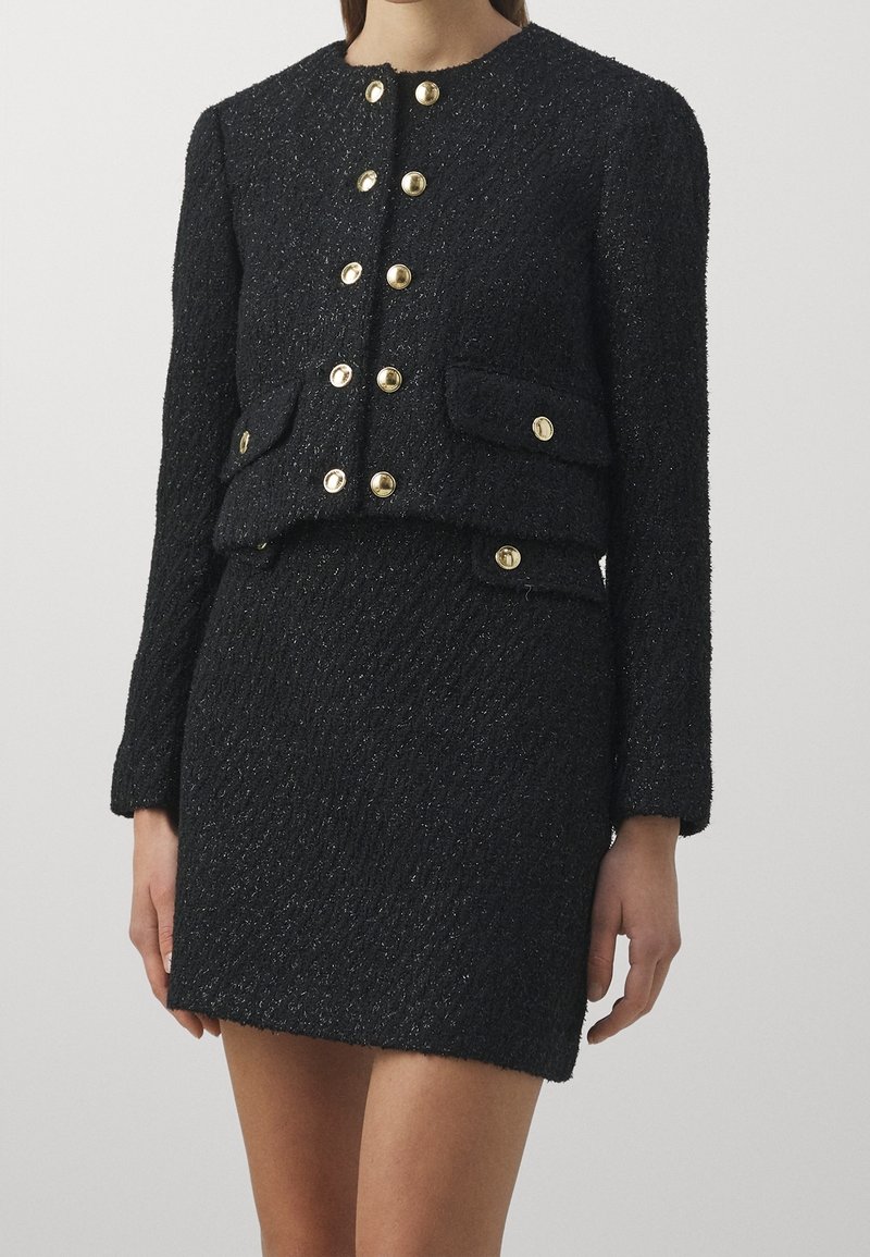Ensemble texturé noir en deux pièces avec des boutons dorés, comprenant une veste courte à poches à rabat et une mini-jupe taille haute assortie.