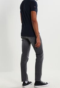 Námořnické tričko s krátkým rukávem, slim fit, v kombinaci se šedými zúženými džíny a černými vysokými teniskami, pohled zezadu.