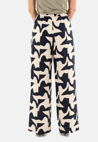 Pantalones de pierna ancha con una base cremosa y un atrevido patrón abstracto en azul marino. Cintura elástica para mayor comodidad y un ajuste relajado. Textura de tela suave.