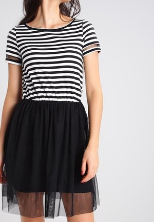 Haut rayé noir et blanc à manches courtes, associé à une jupe en tulle noire. La jupe a une texture semi-transparente en couches.