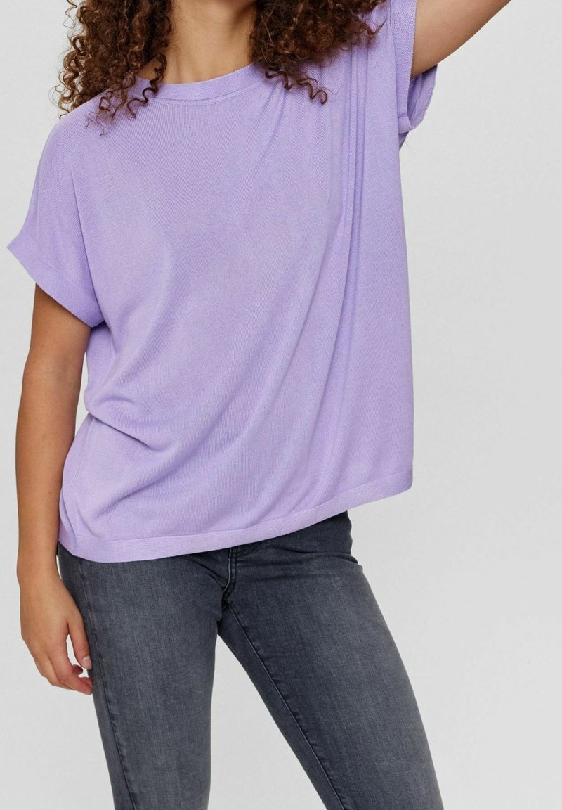 Lös passform lilafärgad t-shirt med korta ärmar och rund halslinning. Tyget verkar mjukt och något texturerat. Bärs med mörkgrå jeans.