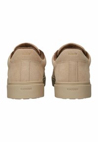 Zapatillas de deporte de ante beige con un acabado texturizado, puntera redonda, collar acolchado y suela de goma marrón; marca en dorado en la parte trasera.