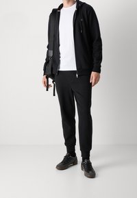 Svart zip-up hoodie, vit t-shirt, svarta sweatpants och mörka sneakers. Enkelt design, jämn textur och figurnära passform. Inkluderar en axelväska.