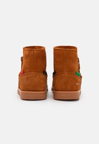 Botas de tobillo de ante marrón con una textura suave, suelas de goma y un pequeño lazo en el lado. Presentan etiquetas de la marca coloridas en los laterales.