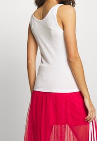 White sleeveless tank top made from ribbed cotton, featuring a scoop neckline. Worn with a sheer, pink tulle skirt.