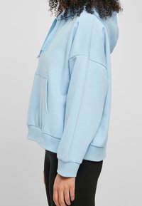 Ljusblå hoodie i mjukt material, med en framficka, dragsko i huvan samt ribbade muddar och nederkant.