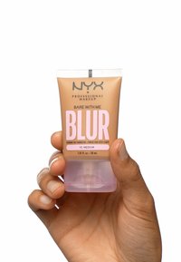 NYX Bare With Me Blur foundation in een zachte beige tube met roze accenten en een doorschijnende roze basis, vastgehouden in een hand. 30 mL formaat.