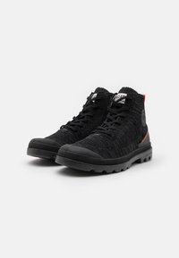 Chaussures montantes noires en mesh texturé avec semelles en caoutchouc. Elles disposent d'un bout renforcé et d'un petit accent orange près du talon.