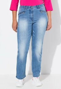 Jeans de mezclilla azul claro con un corte holgado, que cuentan con bolsillos delanteros y un ligero desvanecimiento. Combinados con zapatillas blancas y una blusa rosa.