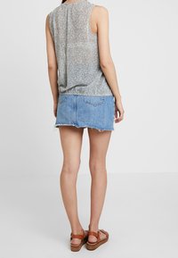 Top sin mangas de flores, tela ligera, en tonos gris y pastel, combinado con una falda corta de mezclilla azul con dobladillo deshilachado y dos bolsillos traseros.