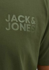 Oliven grønn bomull t-skjorte med en subtil preget logo "JACK & JONES" i lysere grønt på forsiden, med en jevn tekstur.