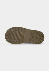 Semelle de botte en caoutchouc marron avec un profil profond pour la traction, vue du dessous sur un fond uni.