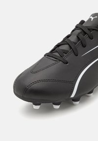 Scarpini da calcio neri realizzati in materiale sintetico, con una texture liscia, dettagli bianchi e una suola sagomata con tacchetti bianchi.
