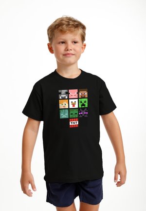 Černé tričko s krátkým rukávem, které zobrazuje pixelovou kresbu postav v mřížkovém vzoru, včetně krávy, prasete, kuřete a loga TNT.